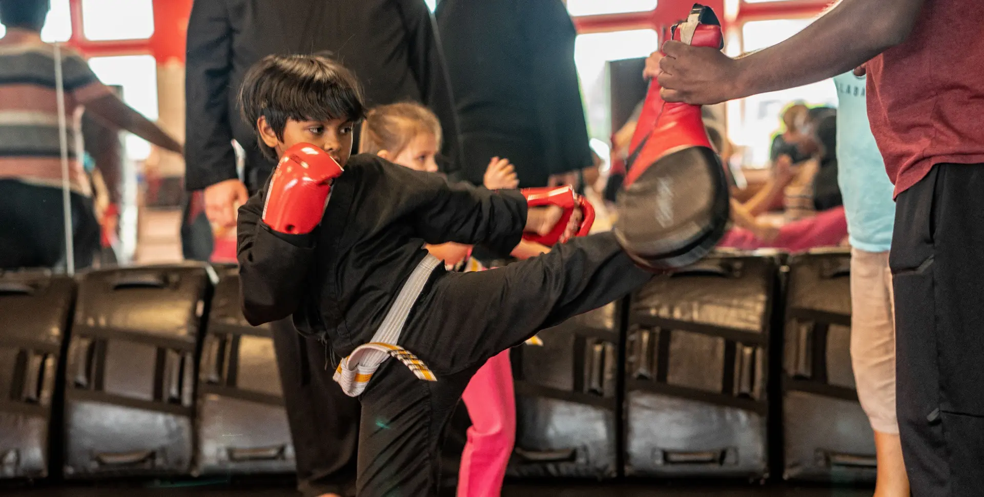 A young boy is kicking around with his red boxing gloves.